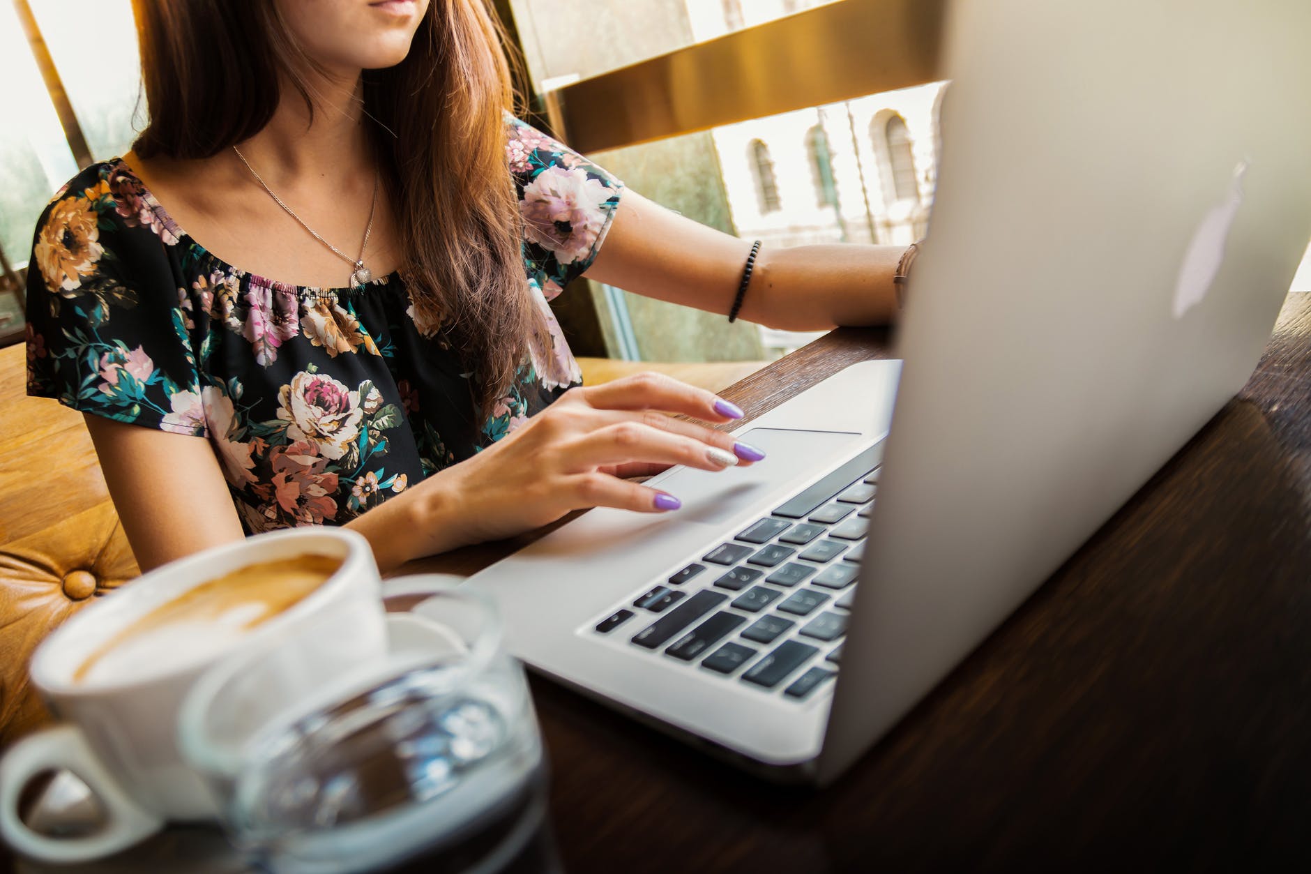 woman wearings coop neck floral top using her apple brand macbook